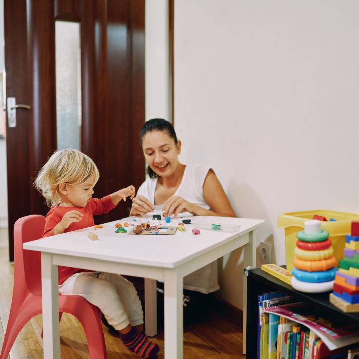 Mom with a little girl sculpt plasticine sitting at a table in the room. High quality photo